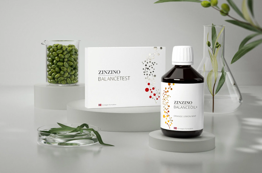 Counter displaying a bottle of Zinzino BalanceOil and a box of the BlanceTest, with a glass beaker of green oilves and another glass beaker with water and an olive branch.